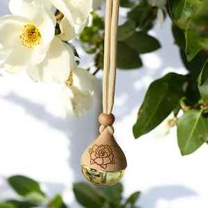 May include: A wooden car air freshener with a floral design hanging from a white string. The air freshener is shaped like a teardrop and has a clear glass vial inside.