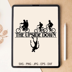 Peut inclure: Un graphique numérique sur un écran de tablette présentant des silhouettes noires de personnages à vélo au-dessus du texte THE UPSIDE DOWN, avec une silhouette de créature inversée en dessous. Le bas de l'écran affiche SVG - PNG - JPG - EPS - DXF.