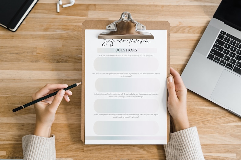 May include: A clipboard with a checklist titled "Self-Criticism Questions". The checklist includes four questions about self-criticism and its impact on life. A person is holding the clipboard and writing on it with a pencil.