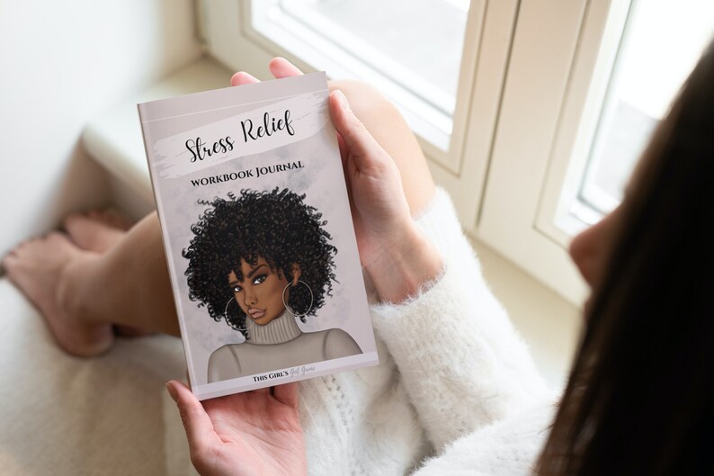 Peut inclure: Une femme tient un journal de travail pour le soulagement du stress avec une illustration color&eacute;e d'une femme sur la couverture. Le texte de la couverture est "Stress Relief Workbook Journal" et "This Girl's Got This".