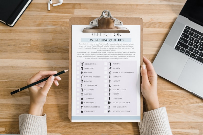 May include: A clipboard with a printed list titled "REFLECTION ON ENDURING QUALITIES" is held by a person. A pencil rests on the list. A laptop and notebook are on the wooden surface.