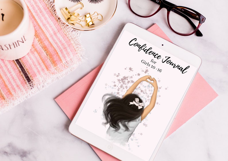 May include: A white tablet with a pink and white striped background. The tablet screen displays a digital journal cover with a girl with long black hair making a heart shape with her hands. The text on the cover reads "Confidence Journal for Girls 10-16".