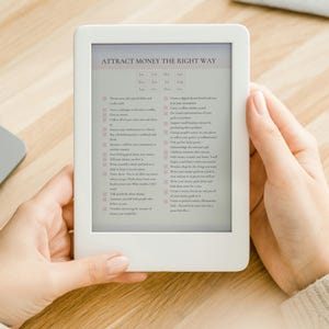 May include: A white e-reader with a gray screen displaying a list of tips titled "Attract Money The Right Way".