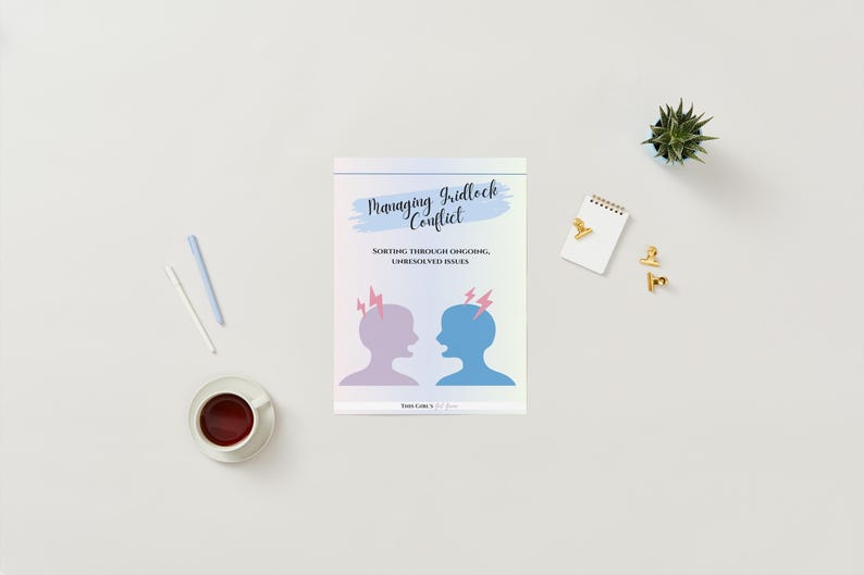 May include: A book titled "Managing Gridlock Conflict" with illustrations of two silhouetted heads with lightning bolts. The book is on a white surface with a cup of coffee, pens, a notepad, and decorative gold paper clips.