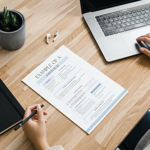 May include: A workspace with a laptop, a printed safety plan, a notebook, and a small potted plant. The safety plan has text and is on a wooden desk. A person is using the laptop and writing on the plan.