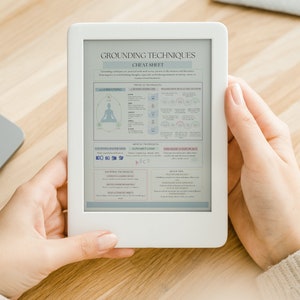 May include: A white e-reader displaying a "Grounding Techniques Cheat Sheet" with text and diagrams. The device is held by a person, with a laptop visible in the background. The e-reader's screen shows information about grounding exercises.