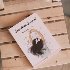 May include: Pink and white journal with the title "Confidence Journal for Girls 10-16" and an illustration of a girl with long brown hair making a heart shape with her hands. The background is a light pink with white stars.