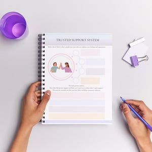 May include: A spiral bound notebook with a purple and white cover. The cover has the text "Trusted Support System" and an illustration of two people giving each other a high five. The notebook is open to a page with a chart for listing names and how they support you.