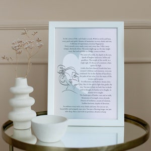May include: White framed art print with a black and white line drawing of two faces. The print features a quote about life, experiences, and the beauty of each moment. The print is on a table with a white ceramic vase and bowl.