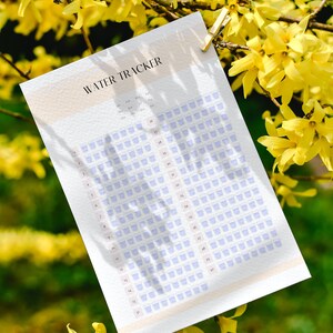 May include: A printable water tracker with a light peach background and a grid of blue water glasses. The tracker is labeled "WATER TRACKER" and includes months of the year from January to December.
