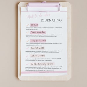 Puede incluir: Una lista de verificaci&oacute;n con un portapapeles rosa y una hoja de papel blanca con el t&iacute;tulo "Qu&eacute; hacer cuando se lleva un diario". La lista de verificaci&oacute;n incluye consejos para comenzar una pr&aacute;ctica de diario, como crear un espacio sagrado, cambiar el entorno, convertirlo en un h&aacute;bito, hacer un seguimiento de tu diario y utilizar diferentes t&eacute;cnicas de diario.