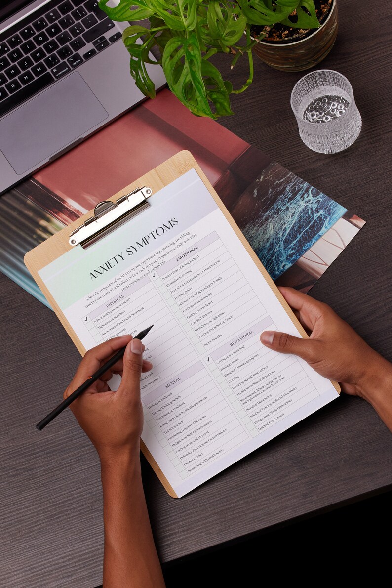 May include: A checklist on a clipboard with the title "Anxiety Symptoms". The checklist includes categories for physical, emotional, mental, and behavioural symptoms. A person is ticking off some of the symptoms.