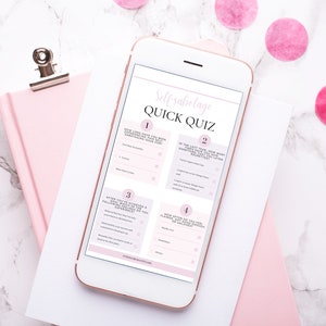 Op de afbeelding: Een witte smartphone waarop een roze en witte snelle zelfsabotagequiz met vier vragen te zien is. De telefoon ligt op een wit oppervlak met een roze notitieboekje en roze confetti.