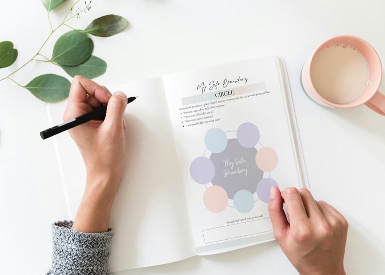 May include: An open journal with the text "My Safe Boundary" and a circle diagram, with a person writing with a black pen. A pink mug with a beverage and green leaves are also visible.