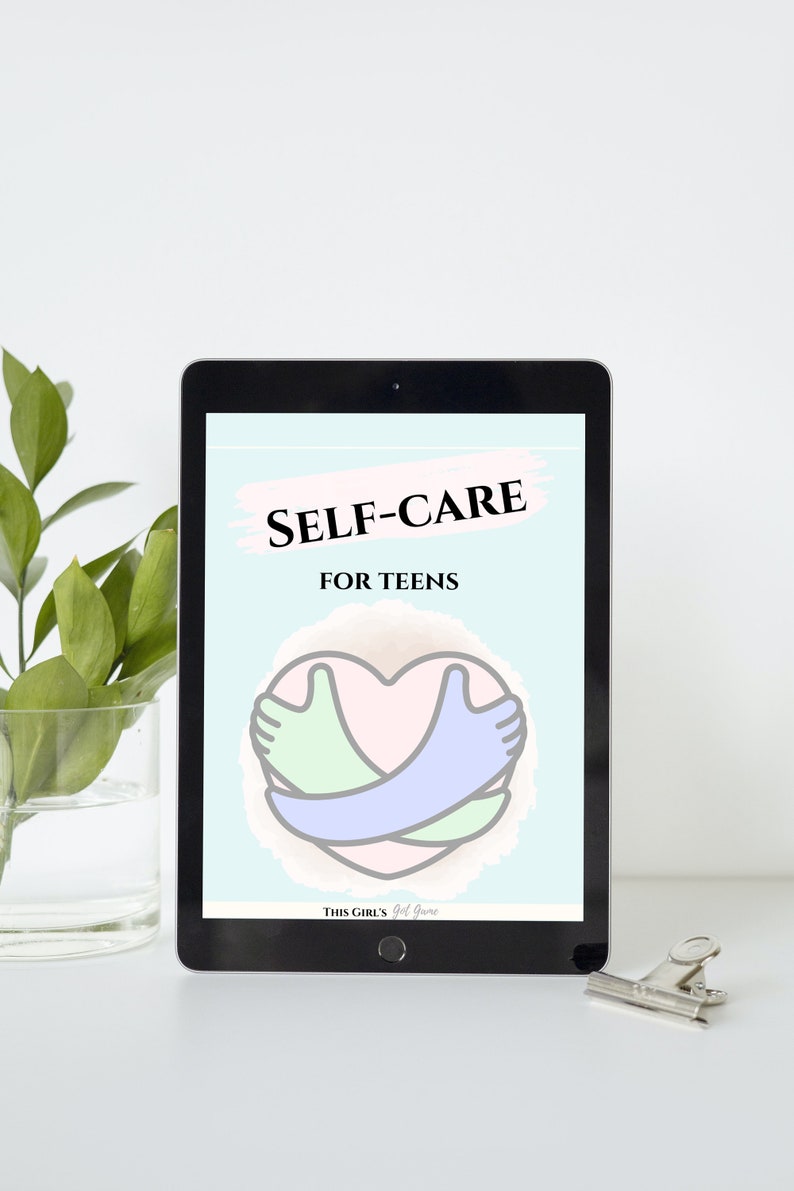 May include: A digital tablet displaying a self-care guide for teens. The guide features a pink heart with two hands embracing it, one green and one blue. The text "SELF-CARE FOR TEENS" is displayed in black text on a light blue background. The bottom of the screen reads "THIS GIRL'S Got Game".