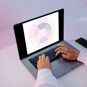 Pu&ograve; includere: Una persona sta lavorando su un computer portatile con un grafico a ruota dei colori visualizzato sullo schermo. Il computer portatile &egrave; su una scrivania bianca con uno smartphone nero accanto.