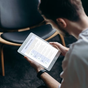 May include: A person is reading a tablet screen with the text "SMART GOAL SETTING" and a table with the acronym SMART. The table lists the criteria for setting effective goals.