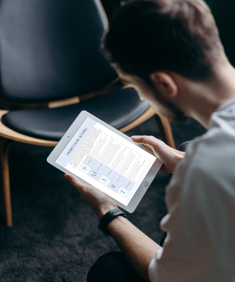May include: A person is reading a tablet screen with the text "SMART GOAL SETTING" and a table with the acronym SMART. The table lists the criteria for setting effective goals.