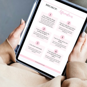 May include: A digital tablet displaying a pink and white breakup affirmations worksheet with six affirmations. The affirmations are numbered 1 through 6 and each affirmation is written in a pink box with a white border. The tablet is being held by a person's hand.