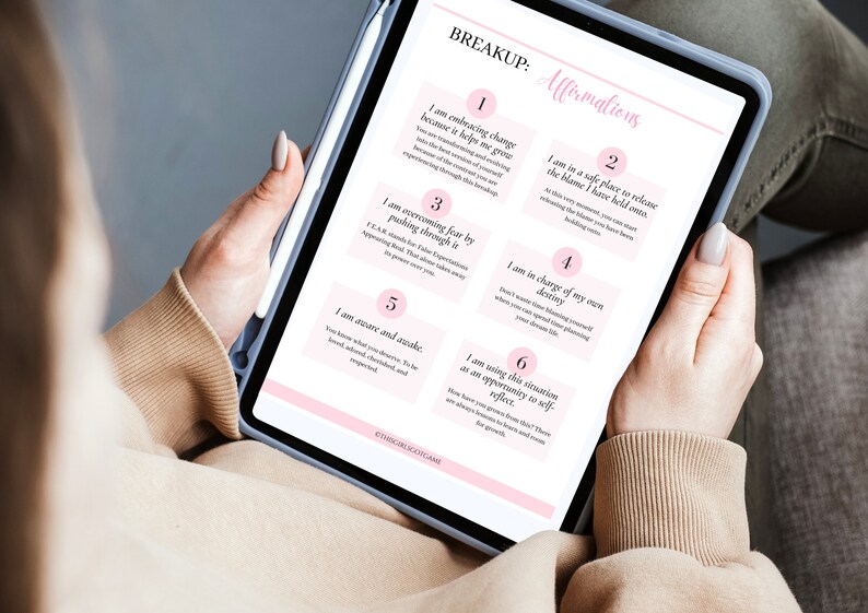 May include: A digital tablet displaying a pink and white breakup affirmations worksheet with six affirmations. The affirmations are numbered 1 through 6 and each affirmation is written in a pink box with a white border. The tablet is being held by a person's hand.