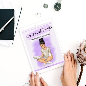 Puede incluir: Una tableta digital que muestra una portada p&uacute;rpura y blanca con el texto "365 Journal Prompts for Positive Thinking". La portada presenta una ilustraci&oacute;n de una persona sentada con un libro y una taza.