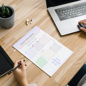 May include: A printable worksheet titled "Legacy and Lessons" with five blank boxes for writing. The worksheet is on a wooden table with a laptop, a notebook, a potted plant, and a pair of earbuds.
