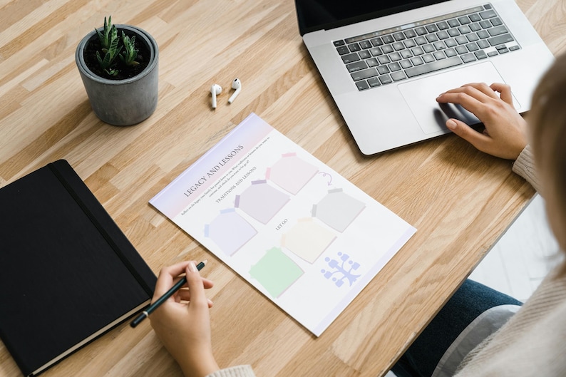 May include: A printable worksheet titled "Legacy and Lessons" with five blank boxes for writing. The worksheet is on a wooden table with a laptop, a notebook, a potted plant, and a pair of earbuds.