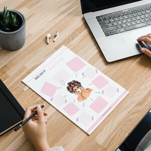 May include: A printable worksheet with the text "BREAKUP: Brainstorming" and a cartoon illustration of a woman with pink hair and a pink background. The worksheet is on a wooden table with a laptop, a potted plant, and a pair of wireless earbuds.