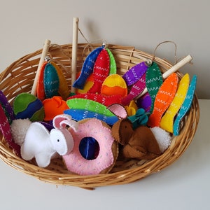 May include: A woven basket filled with colorful felt Easter decorations. The basket contains felt eggs, bunny shapes, donuts, and other festive shapes. The decorations are in various colors, including blue, green, orange, and pink.