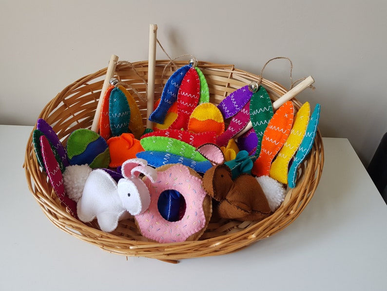 May include: A woven basket filled with colorful felt Easter decorations. The basket contains felt eggs, bunny shapes, donuts, and other festive shapes. The decorations are in various colors, including blue, green, orange, and pink.