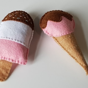 May include: Two handmade felt ice cream treats. One is a pink, white, and brown popsicle with sprinkles. The other is a pink ice cream scoop on a tan cone.