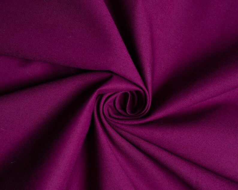 May include: A close-up of a deep purple fabric with a soft, smooth texture. The fabric is folded and draped, creating a swirling pattern.