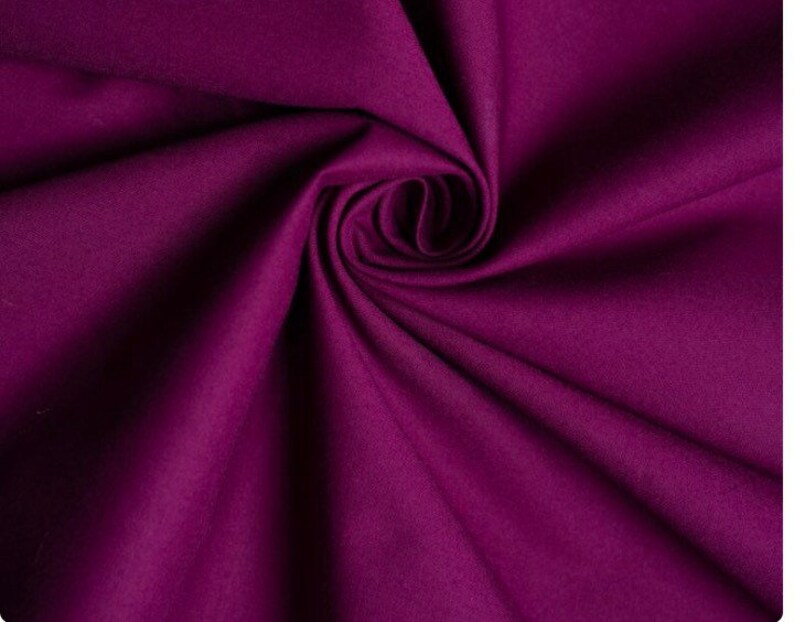 May include: A close-up of a deep purple fabric with a soft, smooth texture. The fabric is folded and draped, showcasing its rich color and luxurious feel.