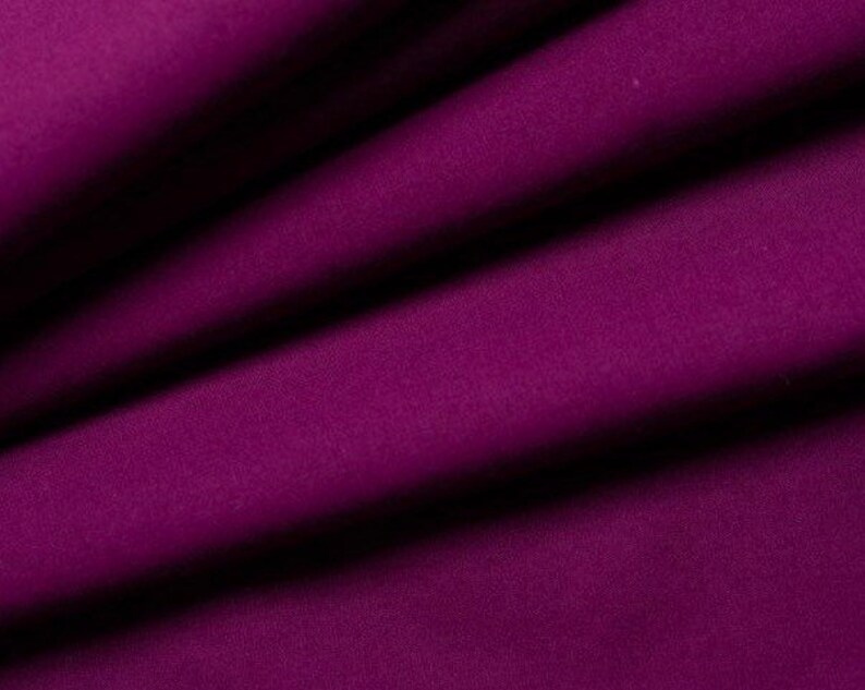 May include: A close-up of a deep purple fabric with a smooth texture. The fabric is folded in a way that shows the drape and flow of the material.