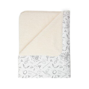 Può includere: Coperta bianca e crema con bordo fantasia. Il bordo presenta disegni a tratto nero di simboli magici, tra cui occhiali, fulmini e un cappello parlante. La coperta ha un interno morbido e felpato color crema.