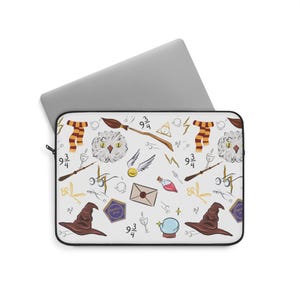 Peut inclure: Housse d'ordinateur portable blanche avec un motif répété d'illustrations sur le thème d'Harry Potter. Le design comprend un chapeau de tri marron, un vif d'or, un balai et une écharpe. Un ordinateur portable argenté est partiellement visible.