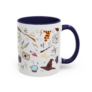 Può includere: Tazza in ceramica bianca con interno e manico blu navy. La tazza è decorata con varie illustrazioni, tra cui una scopa, una sciarpa e un cappello parlante. Il design presenta un motivo ripetuto di elementi magici.