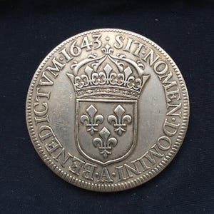 以下が含まれることがあります： 詳細なデザインの銀貨。コインには、3つのフルール・ド・リスが付いたシールドの上に王冠が描かれています。「DICTVM-1643-SIT-NOMEN-DOMINI-A-BENEDICTVM」の文字が縁に刻まれています。コインにはギザギザの縁があります。
