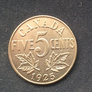Puede incluir: Una moneda canadiense de cinco centavos de bronce de 1925. La moneda presenta la palabra "CANADA" en la parte superior, "FIVE 5 CENTS" en el centro y el año "1925" en la parte inferior. También hay dos hojas de arce.
