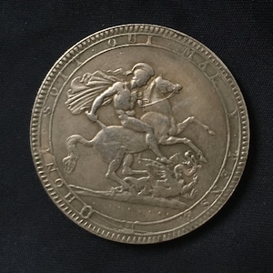 May include: A silver coin showing a man on horseback, spearing a dragon. The coin has a detailed edge with text. The man is wearing a cape. The coin's design is highly detailed and intricate.