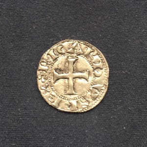 May include: A silver coin with a cross in the centre and a circular inscription around the edge.