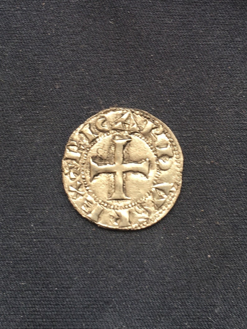 May include: A silver coin with a cross in the centre and a circular inscription around the edge.