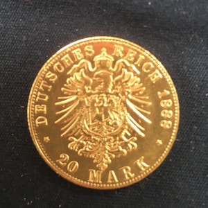 May include: A gold coin with the inscription "Deutsches Reich 1888" and "20 Mark" around the edge. The coin features a German eagle with a crown on its head.