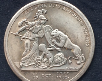 May include: A silver coin with a raised image of a woman holding a spear and a shield, a lion, and a baby. The inscription around the edge reads "NON SINE DIIS ANIMOSUS INFANS". The date "17 OCT. 1777 1781." is inscribed below the image.