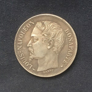 May include: Silver coin featuring a profile portrait of Louis Napoleon Bonaparte, with the inscription "LOUIS-NAPOLEON BONAPARTE" around the edge and "BARRE" at the bottom.