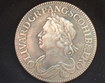 May include: Silver coin with a profile of a person wearing a crown and the text "OLIVARD GR.PANGS CO.HIB.&PRO" around the edge.