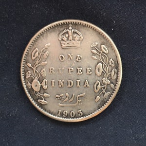 May include: Silver coin with a crown and the text "ONE RUPEE INDIA" and the year "1903".
