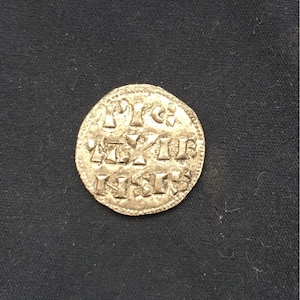 May include: A silver coin with a raised design and inscription. The inscription reads "1113 REX", "1113", and "NSI".
