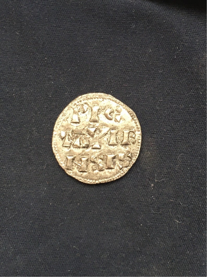 May include: A silver coin with a raised design and inscription. The inscription reads "1113 REX", "1113", and "NSI".