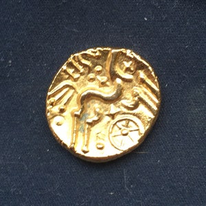 May include: A gold coin featuring a horse and wheel design. The coin is displayed against a dark blue backdrop.